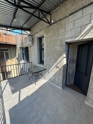 An outdoor balcony with a glass table and chairs, a metal railing, and a concrete wall. - Modern New Apartment- Metro at your door (Երևան)