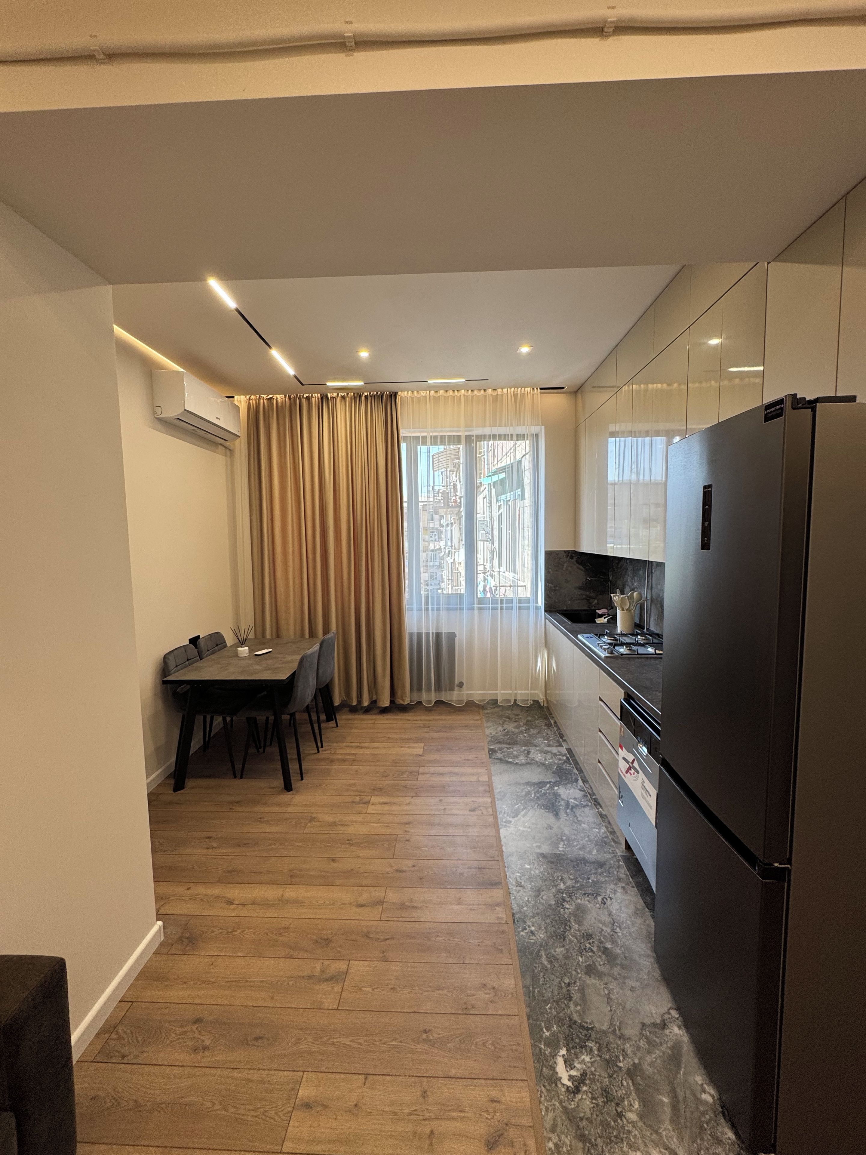 Een moderne keuken met een eethoek, voorzien van een grote koelkast, een fornuis en een eettafel met stoelen.