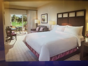Habitación de hotel con una cama grande, un área de descanso con sofá y sillones, y vistas al exterior.