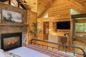 L’intérieur d’un chalet en bois comprend une cheminée, un lit, une salle de bain avec un lavabo et un miroir, ainsi qu’un téléviseur.