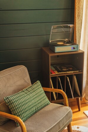 Une pièce avec une chaise en bois, un coussin vert et un tourne-disque posé sur une étagère en bois.