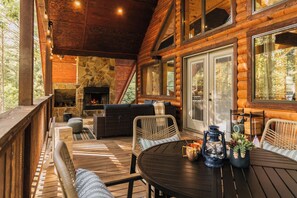 Une terrasse en bois avec des meubles d’extérieur, une cheminée en pierre et une grande fenêtre.