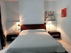 Une chambre d’hôtel avec un grand lit, deux tables de chevet avec des lampes, une tête de lit et un mur orné d’un tableau encadré.