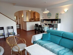 Una sala de estar con sofá, sillas, una mesa de comedor y una cocina al fondo.