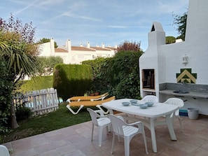 Une terrasse avec une table et des chaises blanches, un barbecue et, en arrière-plan, une vue sur un bâtiment blanc.