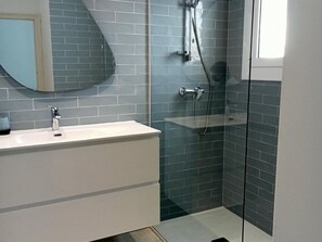 Une salle de bain moderne avec un meuble-lavabo blanc, une cabine de douche en verre et un mur recouvert de carreaux.