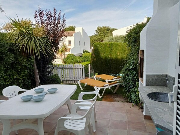 Une terrasse avec une table et des chaises, un transat et un évier en pierre.