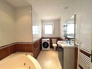 Une salle de bain équipée d’une baignoire, d’un lave-linge, de toilettes et d’un lavabo.