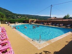 A swimming pool with people in the water, surrounded by lounge chairs and a sandy area.