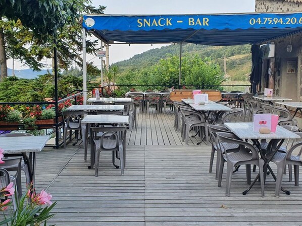 An outdoor seating area with tables and chairs, a covered snack bar, and a view of the surrounding landscape.