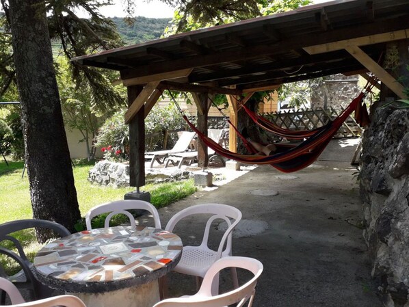 A patio area with a mosaic table, white plastic chairs, a hammock, and a stone wall.