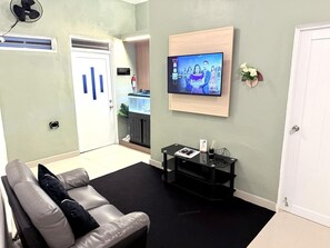 Una habitación con un sofá de cuero, un televisor de pantalla plana en la pared, una mesita con una revista y un tapete de piso negro.