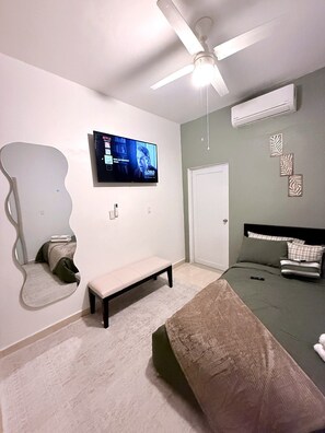 Un dormitorio con una cama, un banco, un televisor montado en la pared y un equipo de aire acondicionado.