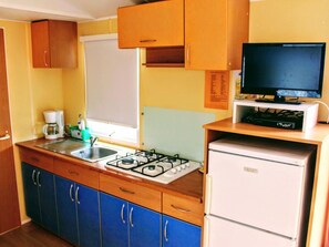 A compact kitchen with a gas stove, a sink, a coffee maker, and a television on a stand. - Cozy mobile home - 4 guests (Verteillac)