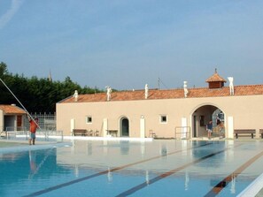Une piscine avec des couloirs bien délimités, un bâtiment doté d’entrées en arc de cercle et d’un toit recouvert de tuiles.