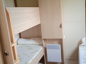 A bunk bed with a mattress featuring a leaf pattern, a white pillow, and a white heater unit. - Cozy chalet with TV - 5 guests (Pleaux)