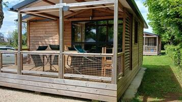 A wooden cabin with a covered porch, a fenced-in area with chairs, and a small deck.