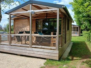 A wooden cabin with a covered porch, a fenced-in area with chairs, and a small deck. - Cozy chalet with TV - 5 guests (Pleaux)