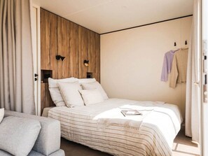 A modern bedroom with a large bed, a wooden accent wall, and a small seating area. - Bungalow, pets allowed - 2 guests (Linguizzetta)