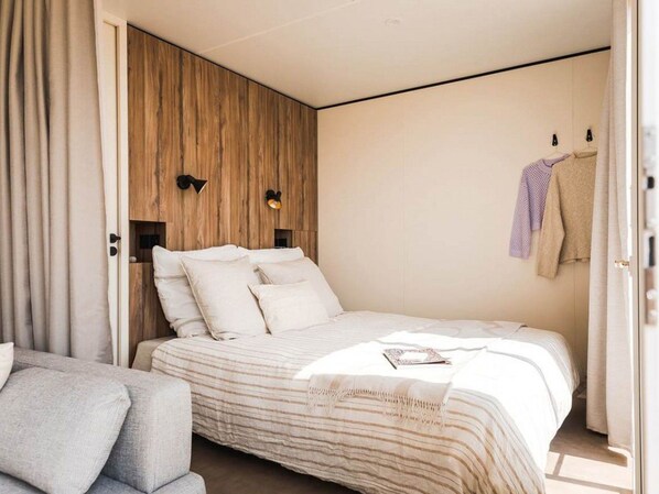 Une chambre moderne avec un grand lit, un mur d’accent en bois et un petit coin salon.