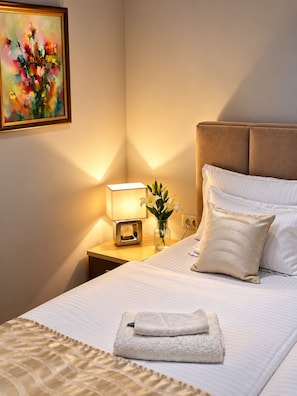 Et hotelværelse med en seng, et natbord, en lampe, en vase med blomster og et billede på væggen.