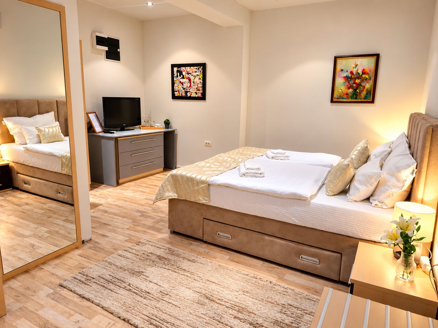 A modern bedroom with a large bed, bedside tables, a desk, a television, and artwork on the walls.