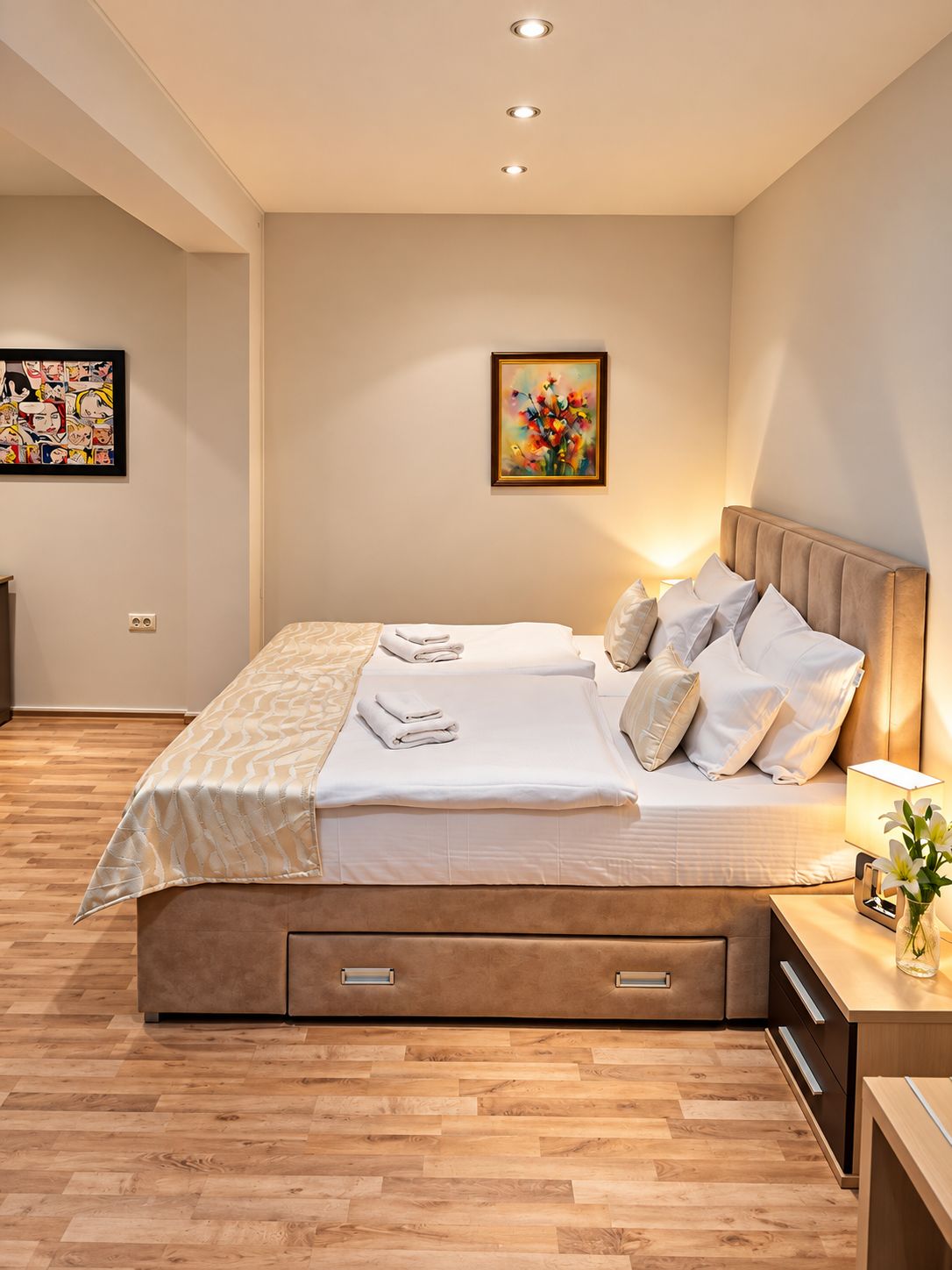 A modern bedroom with a large bed, bedside tables, and artwork on the walls.