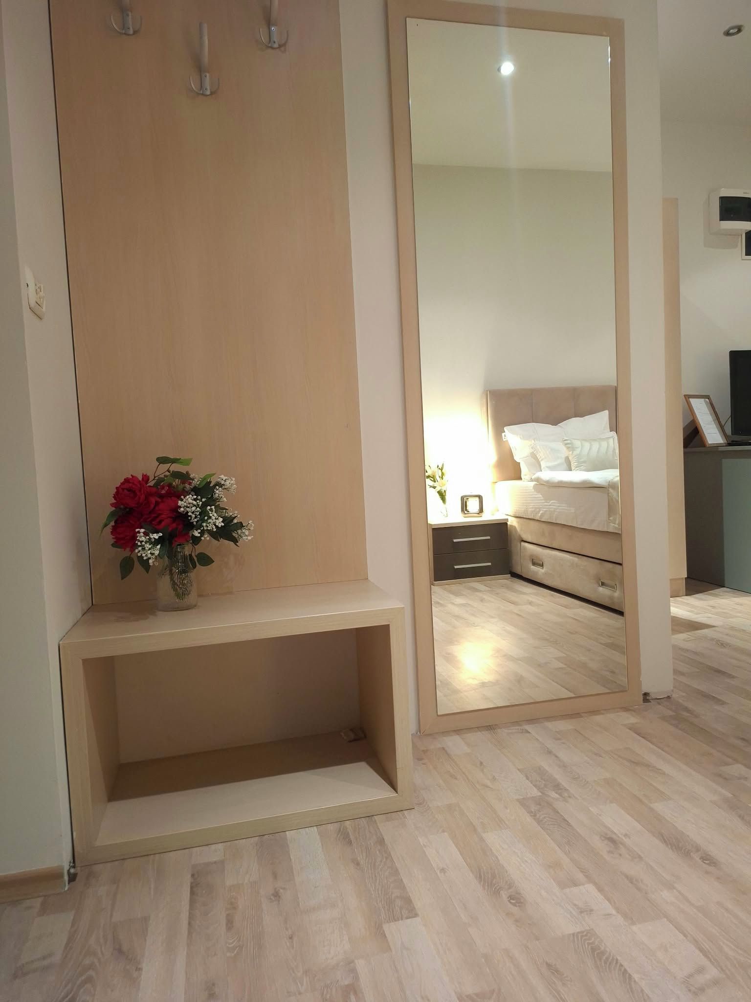 A bedroom with a wooden wardrobe, a bedside table with a vase of flowers, and a bed with white bedding.