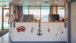 Un comptoir d’accueil avec vue sur la mer, une décoration en forme d’ancre portant l’inscription « Bienvenue » et un panneau « Il est interdit de fumer ».