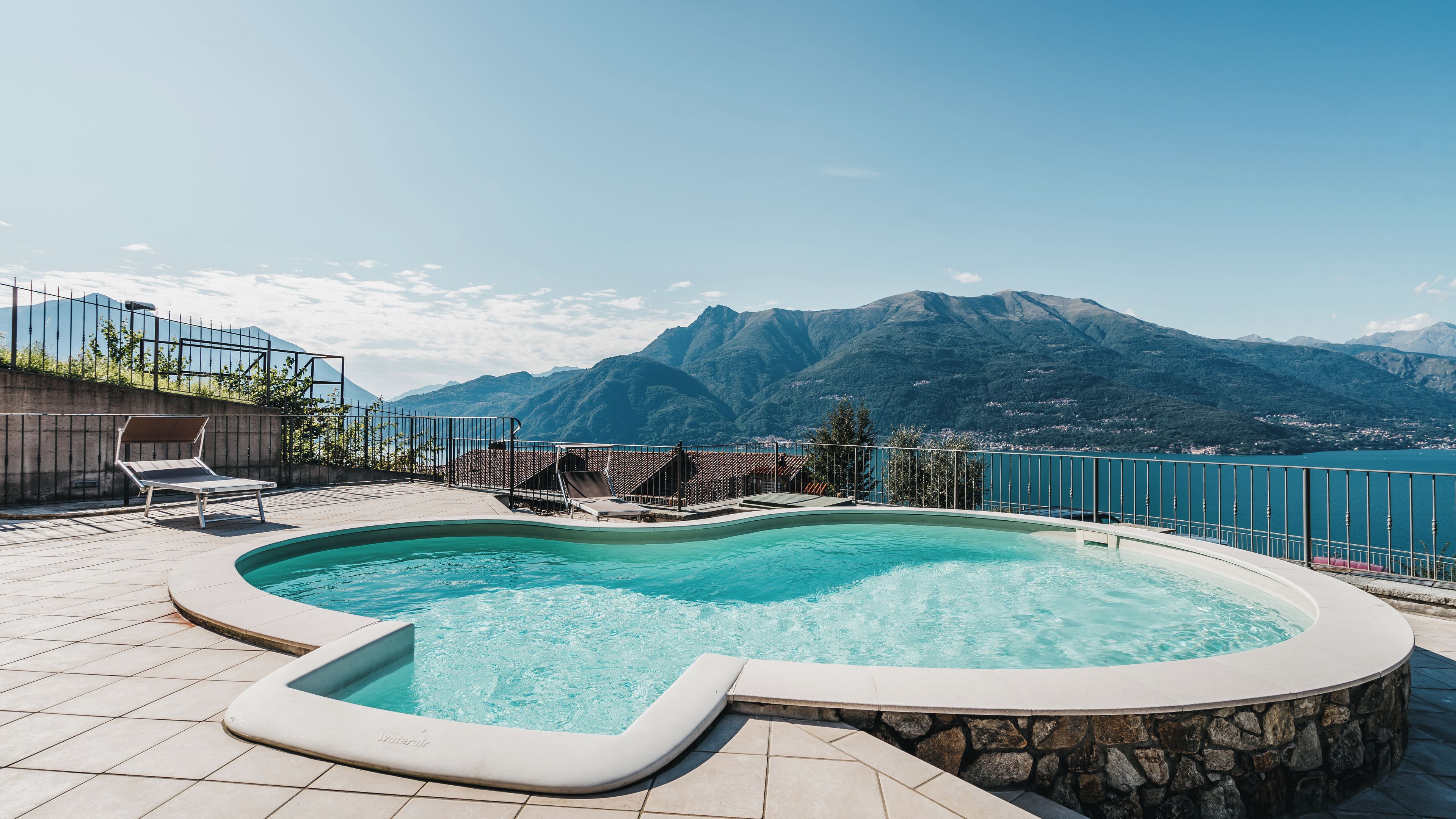 A swimming pool with a mountain view, surrounded by a stone wall and a metal fence.
