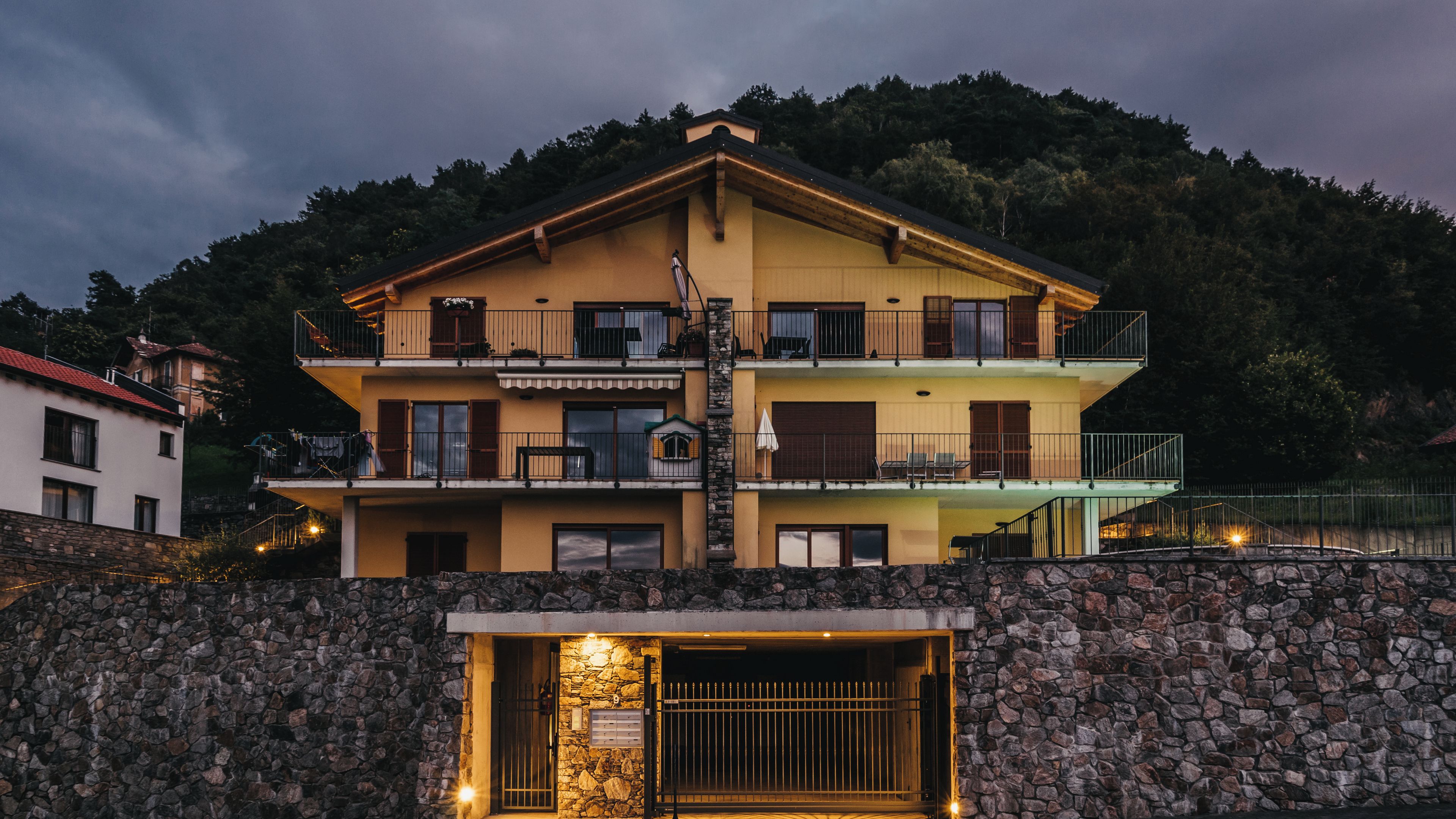 A multi-story building with balconies, a stone wall entrance, and a mountain backdrop.