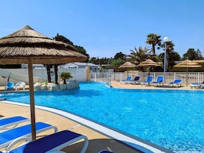 A swimming pool with blue water, surrounded by lounge chairs and thatched umbrellas. - Comfy mobile home, terrace TV - 6 guests (Saint-Hilaire-de-Riez)