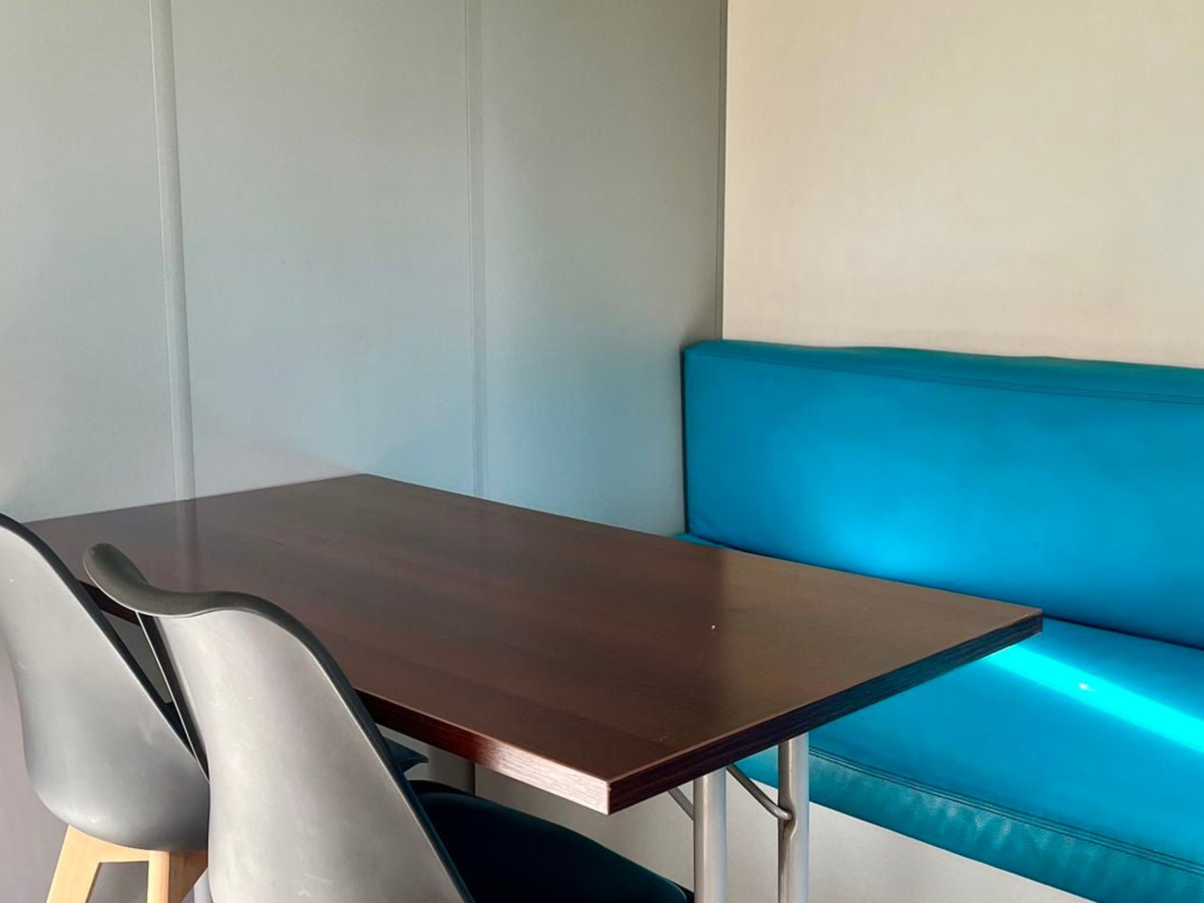 Un coin de pièce avec une table en bois foncé, deux chaises grises et un banc bleu avec un coussin.
