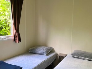 Una piccola camera con un letto singolo, una finestra, un comodino e un cuscino.
