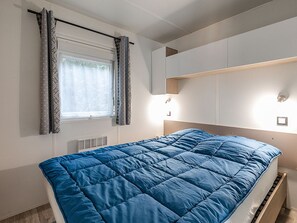 Ein Schlafzimmer mit einem Bett, einem fensterbelaubten Fenster, integrierter Beleuchtung und einem Wandregal.