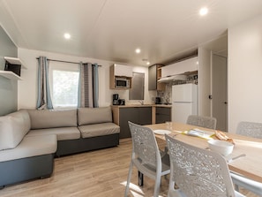 Ein kompakter Wohnbereich mit Sofa, Esstisch, Stühlen, Küchenzeile und einem Fenster mit Vorhängen.