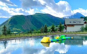 Um lago tranquilo com uma plataforma flutuante, cercado por montanhas e uma cabana de madeira.