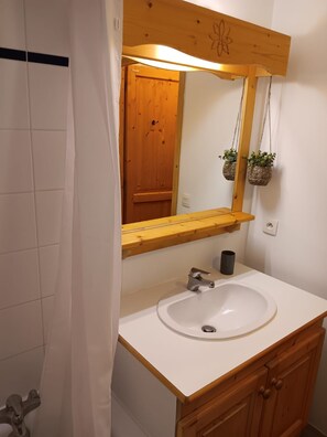 Casa de banho com lavatório branco, armários de madeira, espelho com moldura de madeira e porta de madeira.