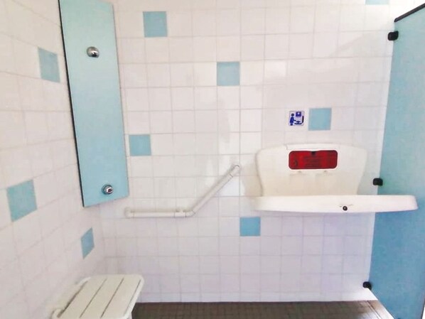Un baño con pared de azulejos blancos y azules, un inodoro blanco con palanca roja para accionar la descarga y un asidero blanco.