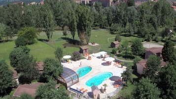 An aerial view of a resort with two swimming pools, surrounded by lush greenery and a large building in the background.