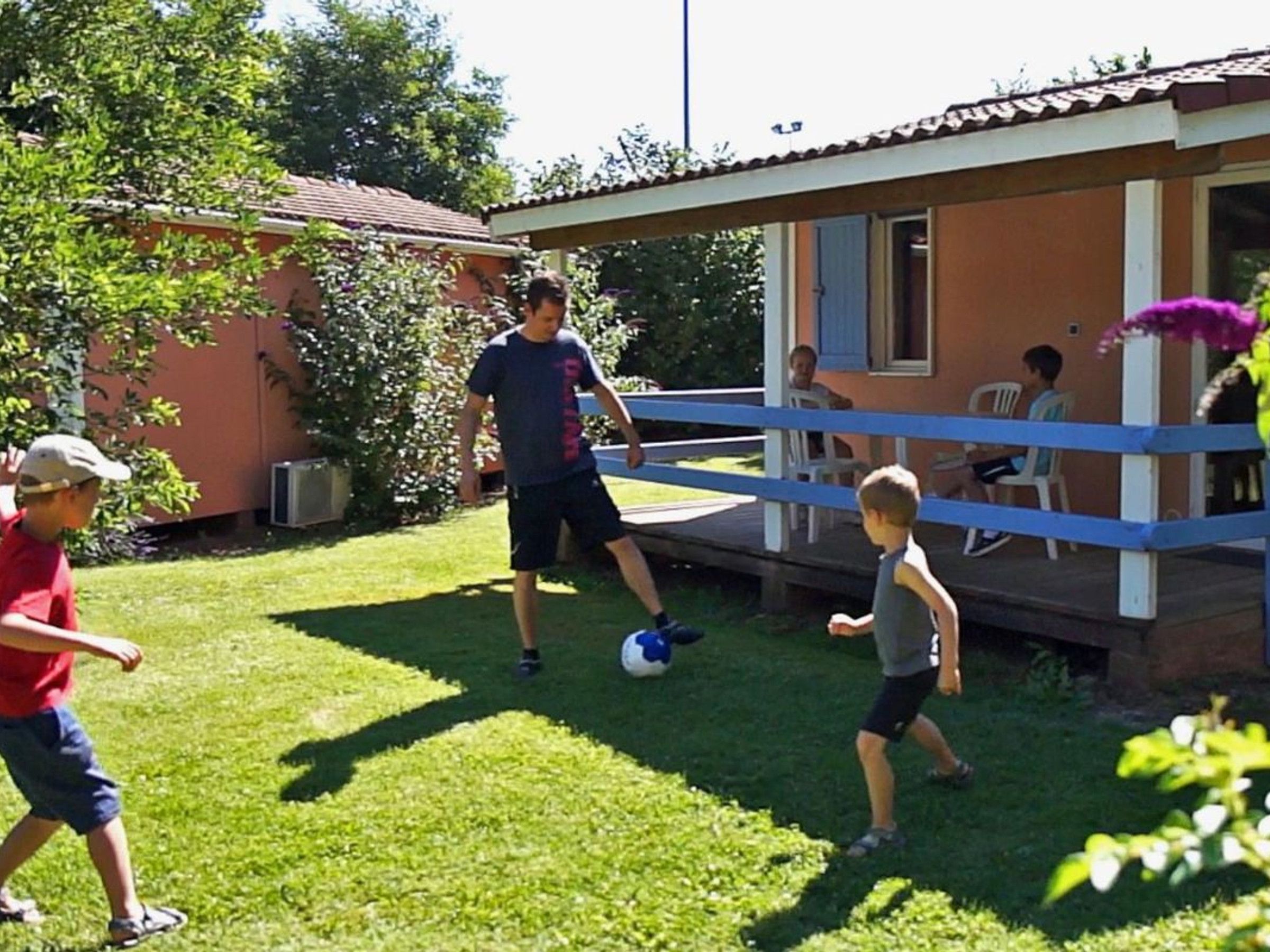 Una casa pequeña con porche, un patio con césped y algunas personas jugando.