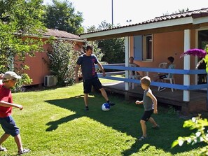Una casa pequeña con porche, un patio con césped y algunas personas jugando.