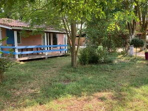 Une petite maison avec un porche et une balustrade bleue. Un arbre se trouve devant la maison.
