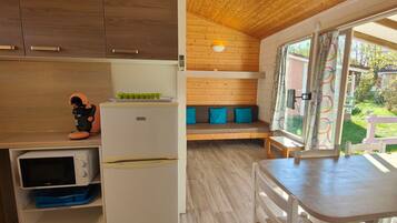 Cocina compacta con microondas, refrigerador y un lavamanos pequeño. En la zona de estar contigua, hay un banco de madera con cojines.