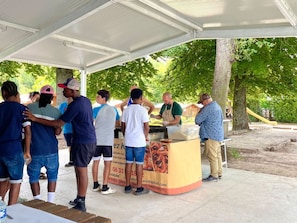 A group of people gathered around a food stall under a covered area with trees in the background. - Mobile home, AC, pets welcome - 2 guests (Angicourt)