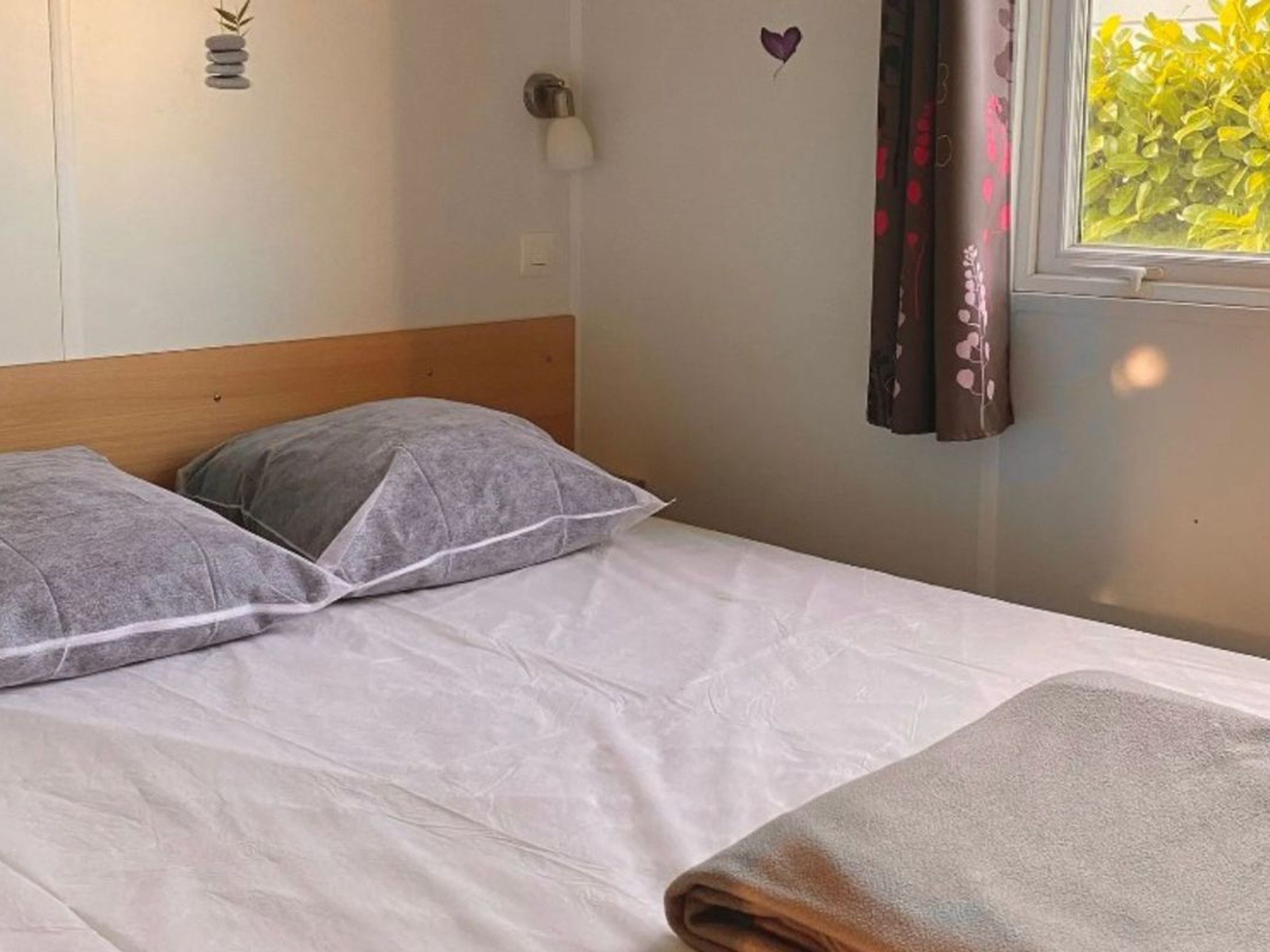A single bed with a wooden headboard, a white bedspread, and two gray pillows.