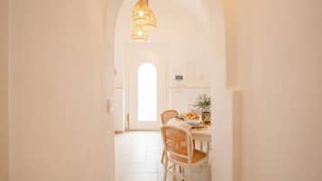 Un comedor luminoso con una mesa blanca, sillas de mimbre y un lámpara colgante.