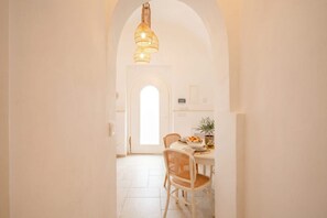 A bright dining area with a white table, wicker chairs, and a hanging light fixture. - La Dimora del Faro | Elegant Suite with Whirlpool Bath (Bari)