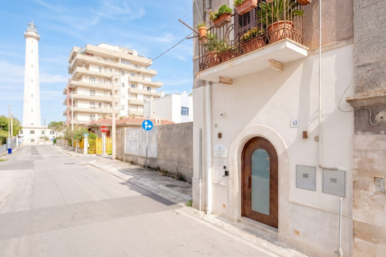 Una calle con un edificio blanco, una señal de stop y un faro a lo lejos.