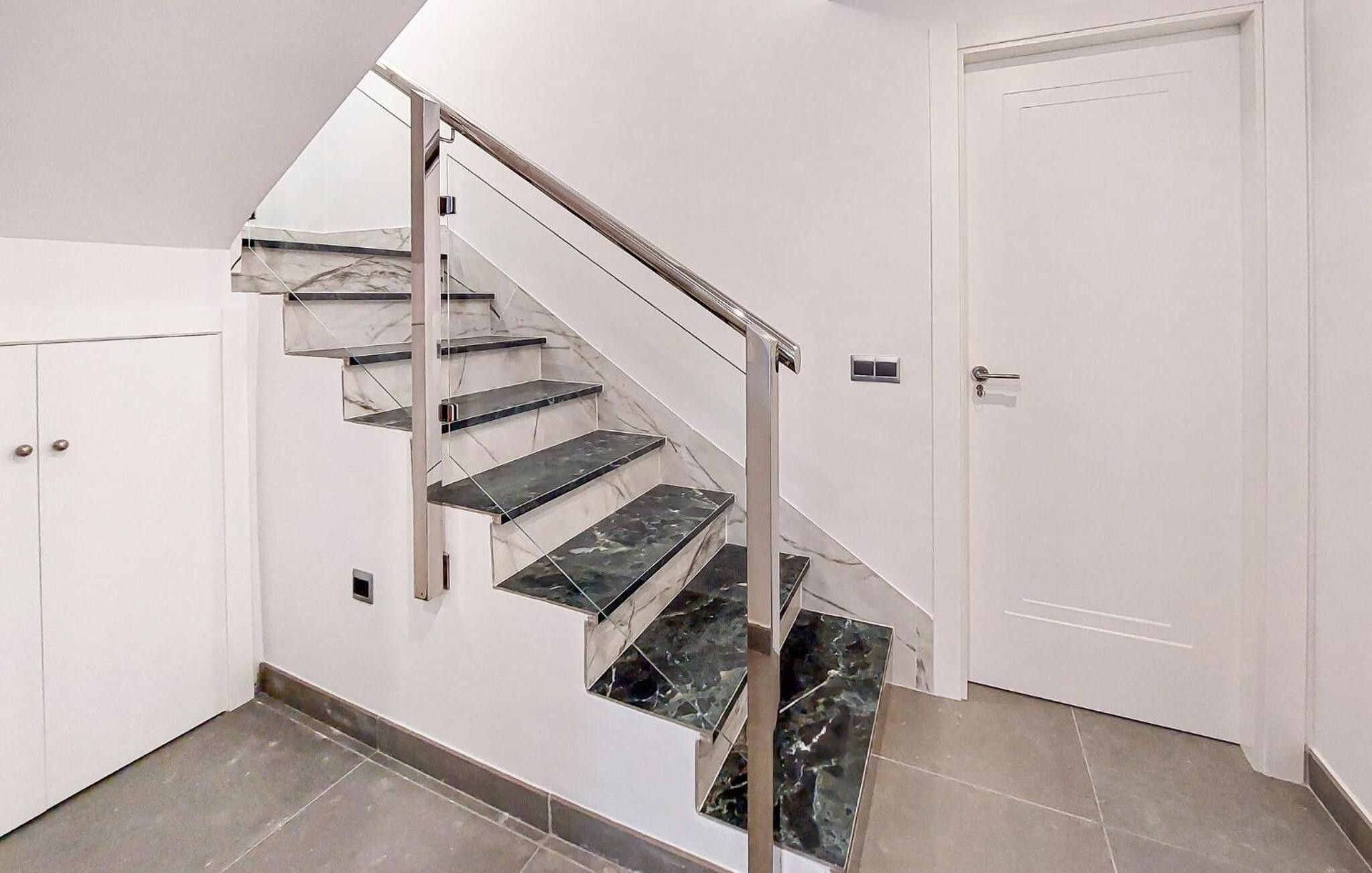 Una escalera con escalones de mármol y barandilla metálica que lleva a una puerta blanca.